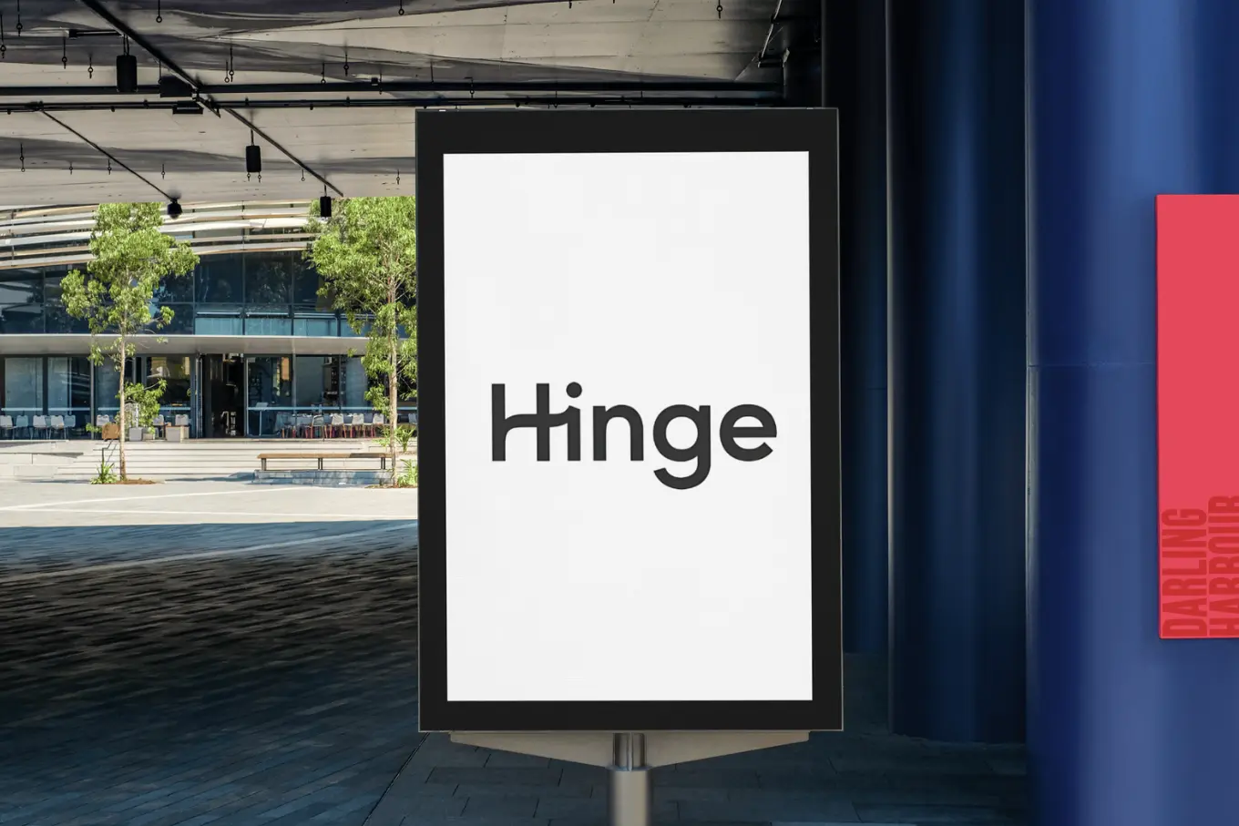 A vertical billboard displaying the word Hinge in black font on a white background. The scene is outside a modern building